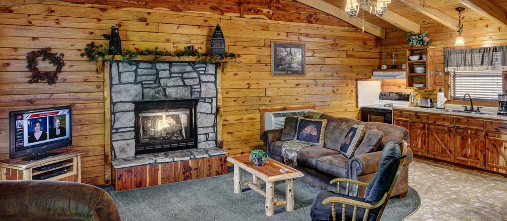 Cabin seating area in front of fireplace with kitchen in the background