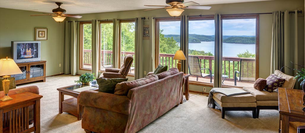 Lakehouse interior seating area with television on. Windows show exterior view of Beaver Lake